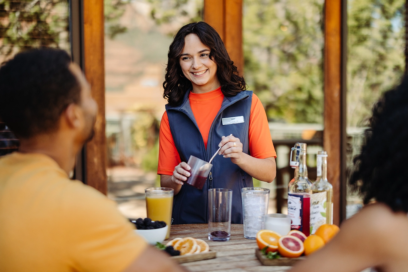 A bartender happily showcases her skills to a pair of guests as she makes a drink