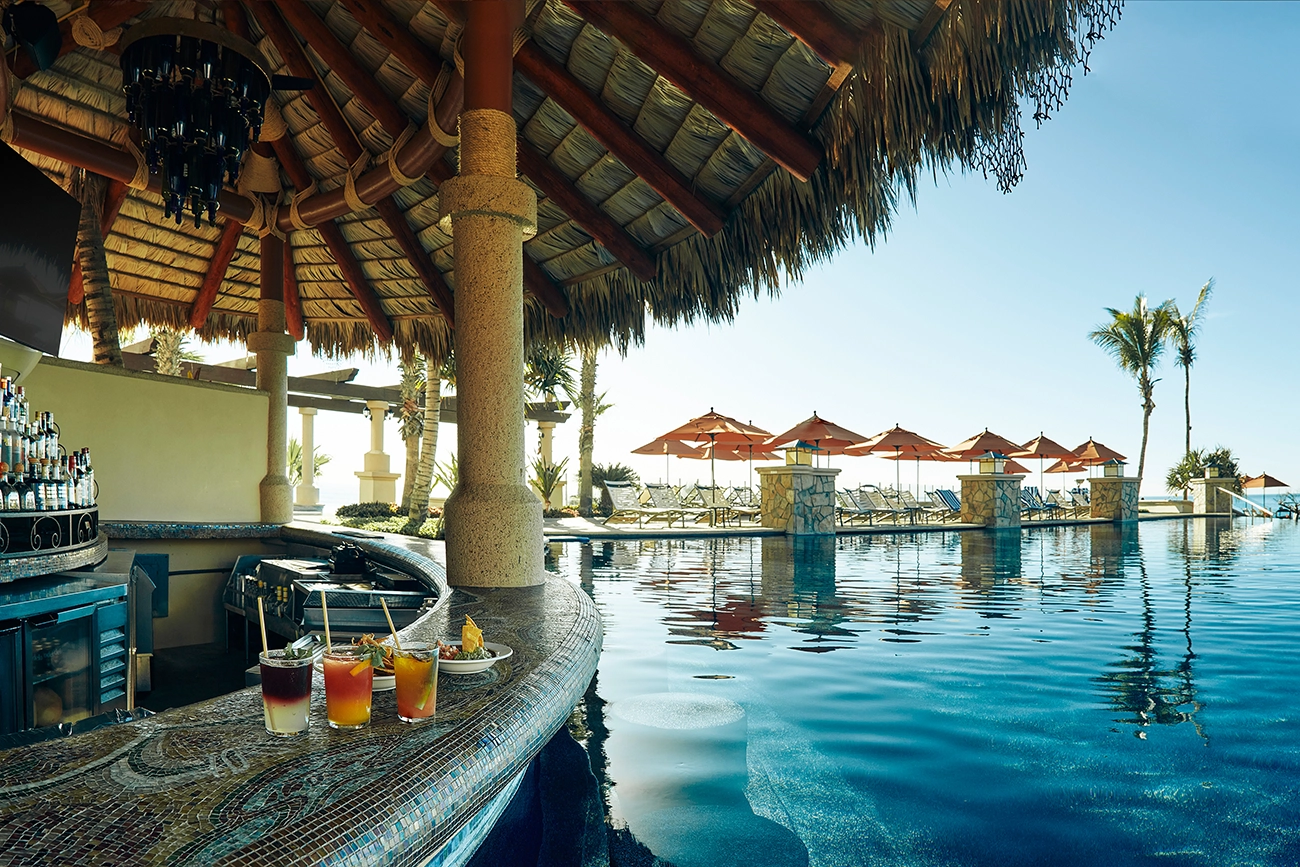 Drinks and food sit on the edge of a poolside, swim-up bar