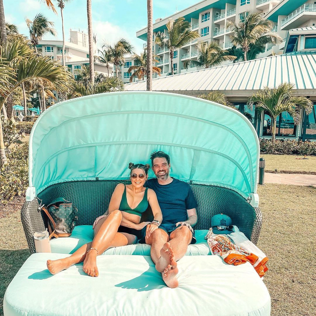 couple sitting on sea foam green outdoor sofa with hotel in background