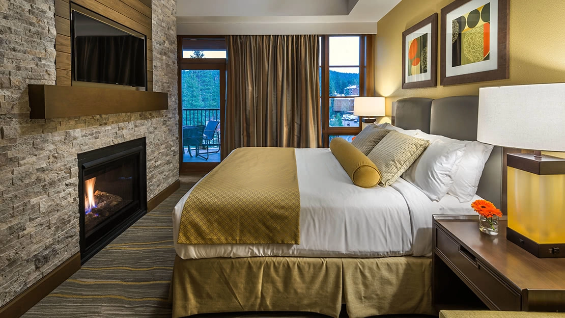 A made bed sits in front of a fire in a resort bedroom