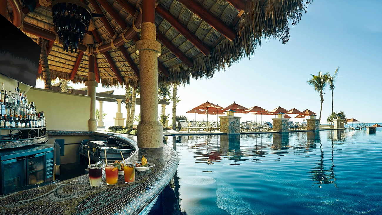 Drinks and food sit on the edge of a poolside, swim-up bar
