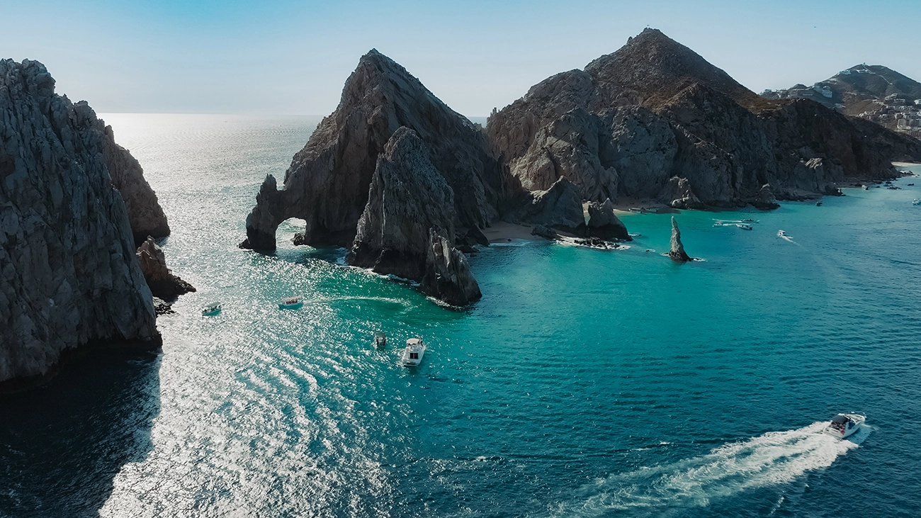 A group of boats sail between rocky outposts in the middle of the blue ocean