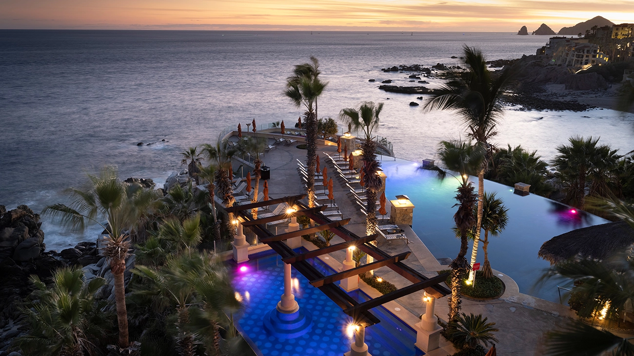A sunset view of an infinity pool, pergola, and ocean