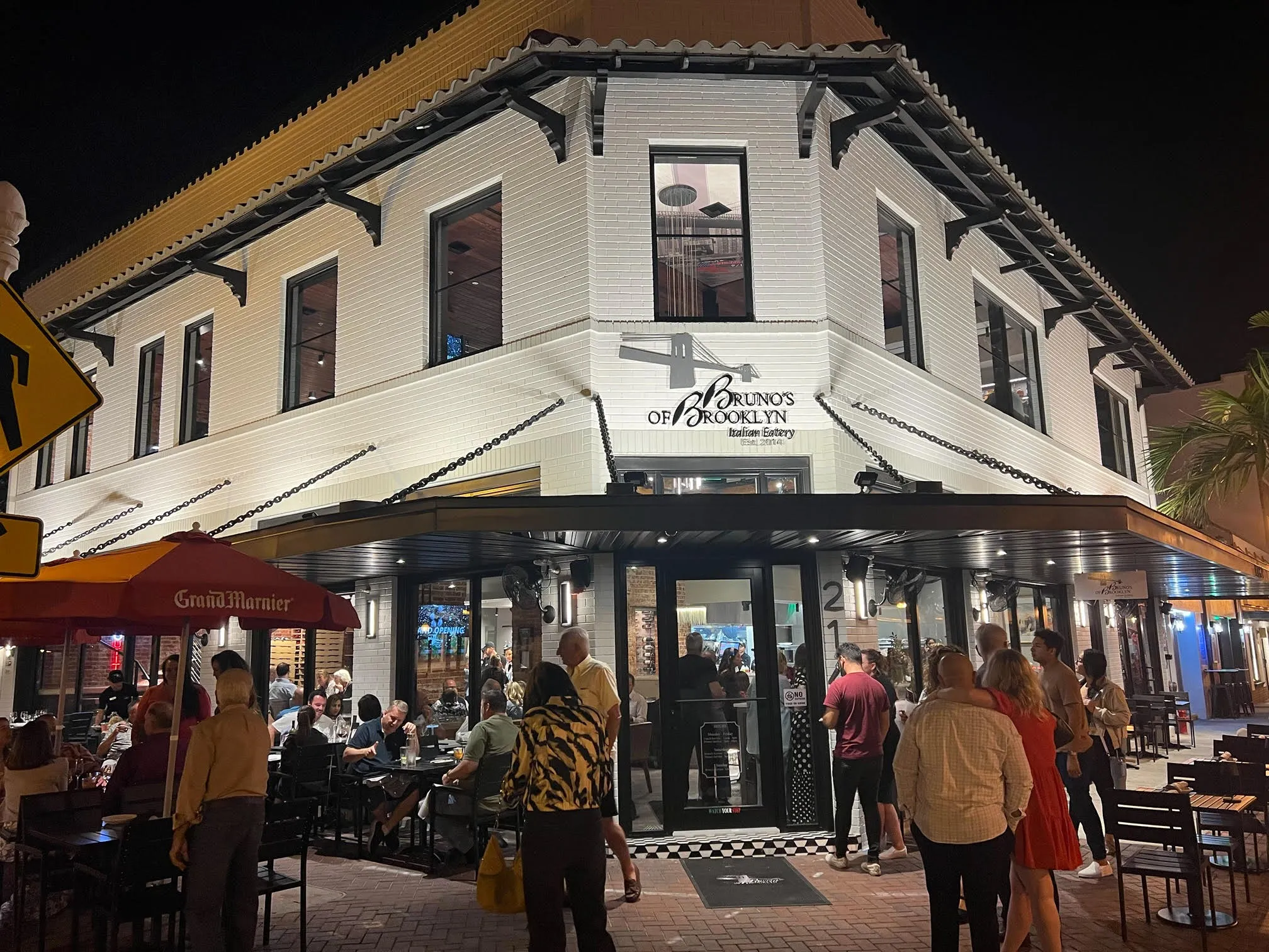 Guests dine outside Bruno’s of Brooklyn restaurant illuminated by warm evening lights.