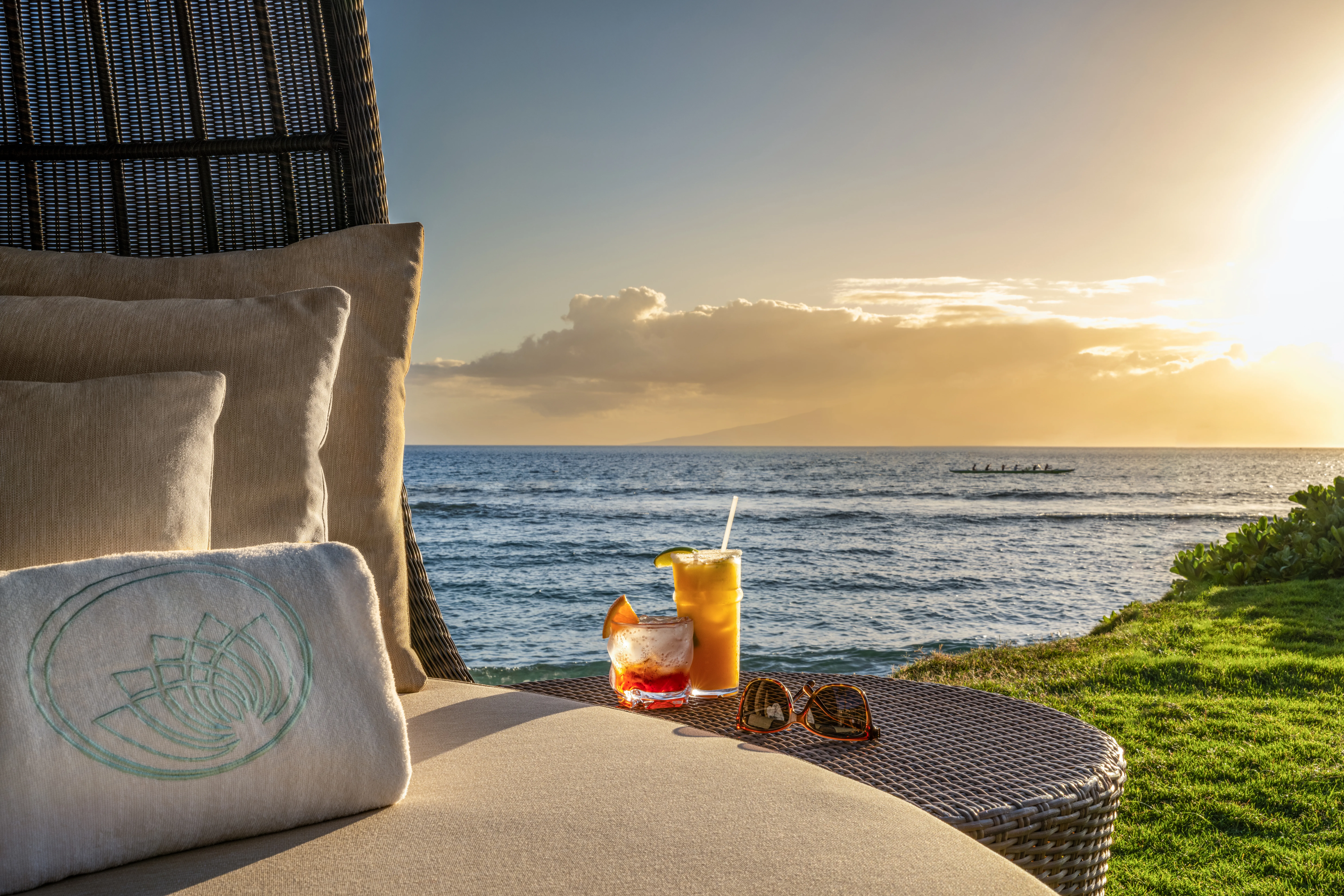 Tropical cocktails on an outdoor table with a panoramic view of Maui’s mountains at sunset.