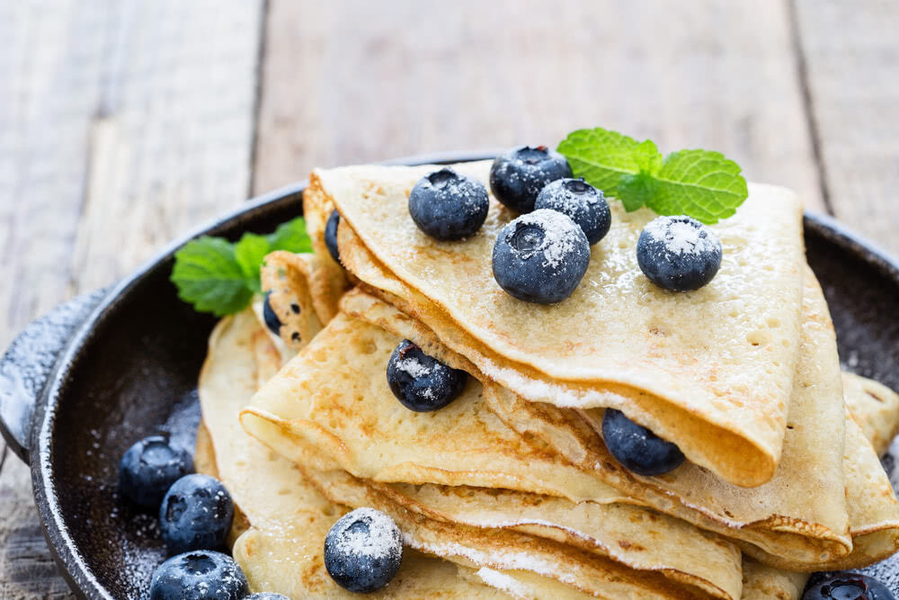 Blueberry crepes stacked on a black plate.