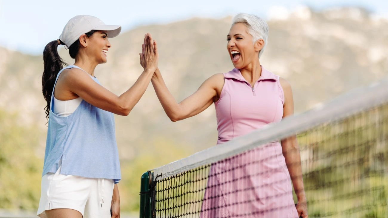 Two pickleball players standing on opposite sides of the net share a high‑five at The Welk.