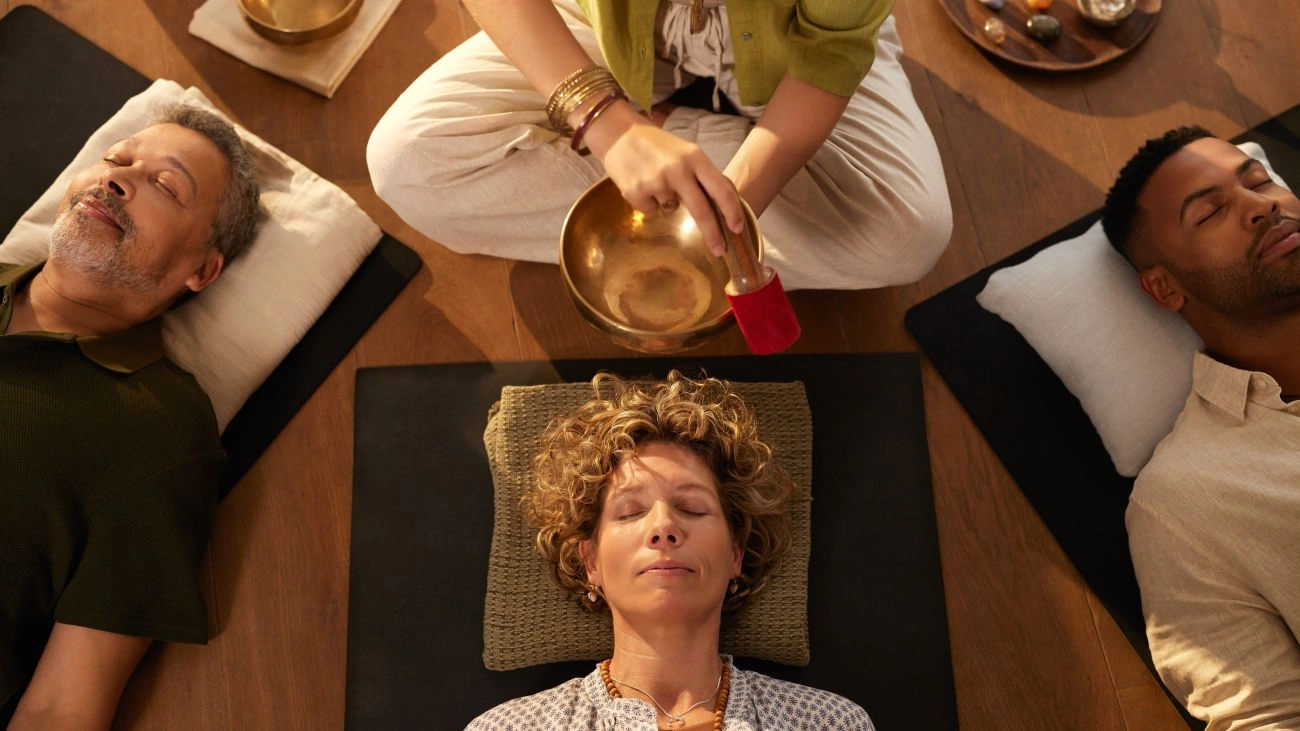 Holistic therapist using a Tibetan singing bowl while group relaxes. 