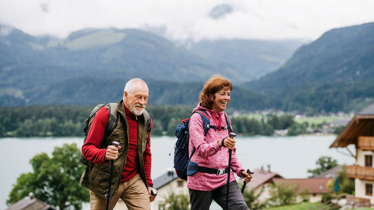 Two hikers with trekking poles walk along a grassy hillside. 