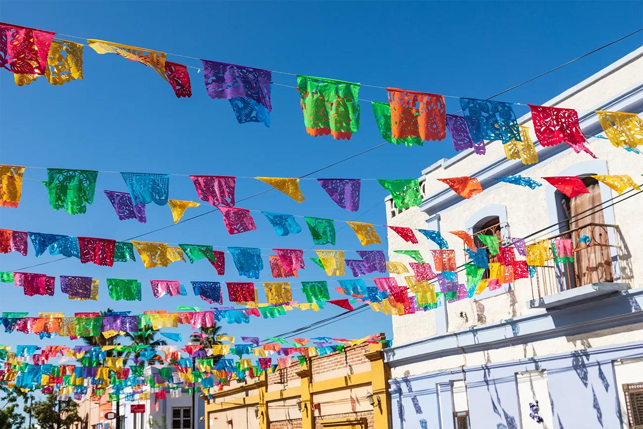 Rows of colored flags hanging between buildings against a blue sky