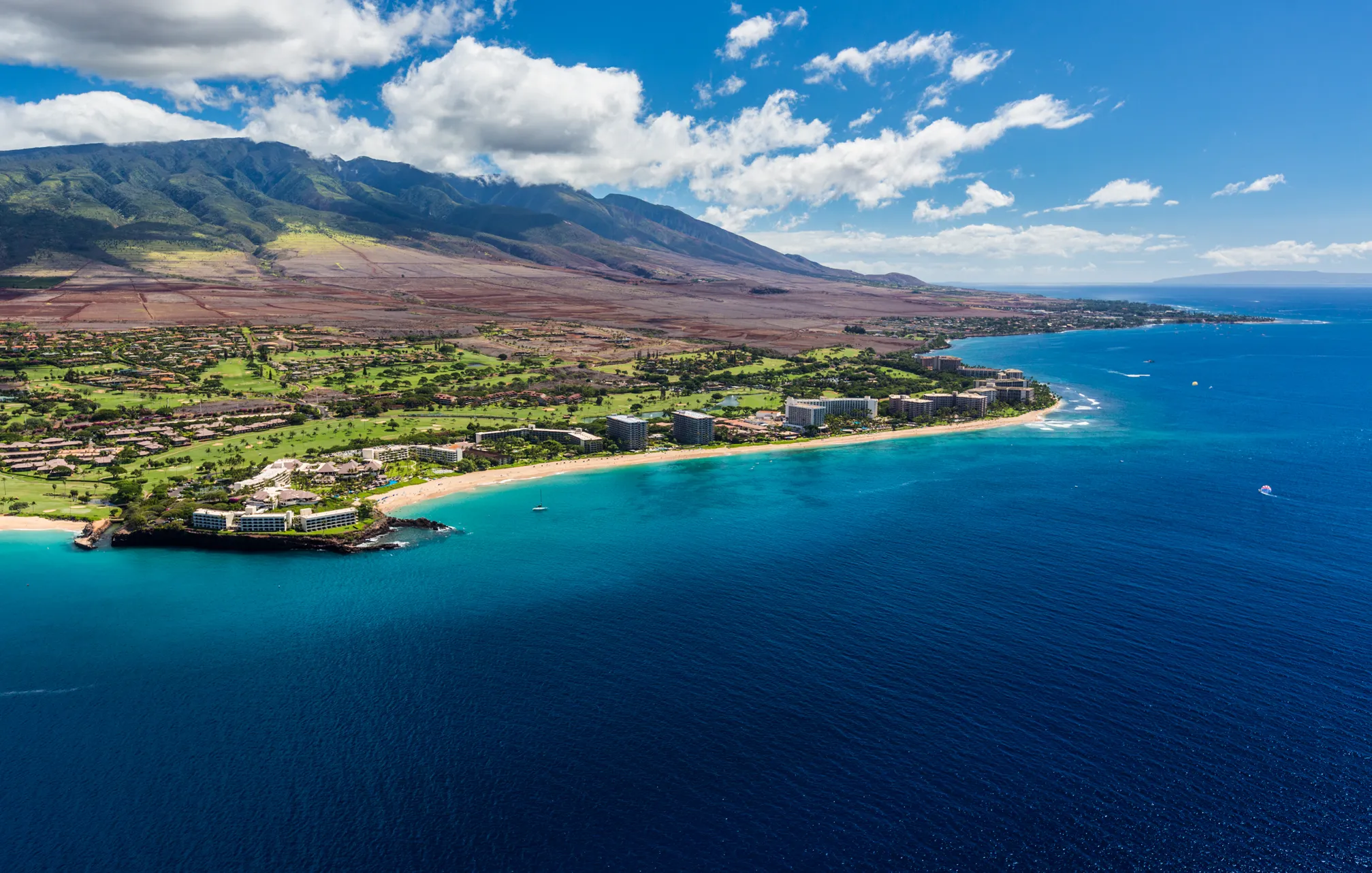 Aerial view of Kā‘anapali Beach showing the coastline, ocean, and lush greenery.