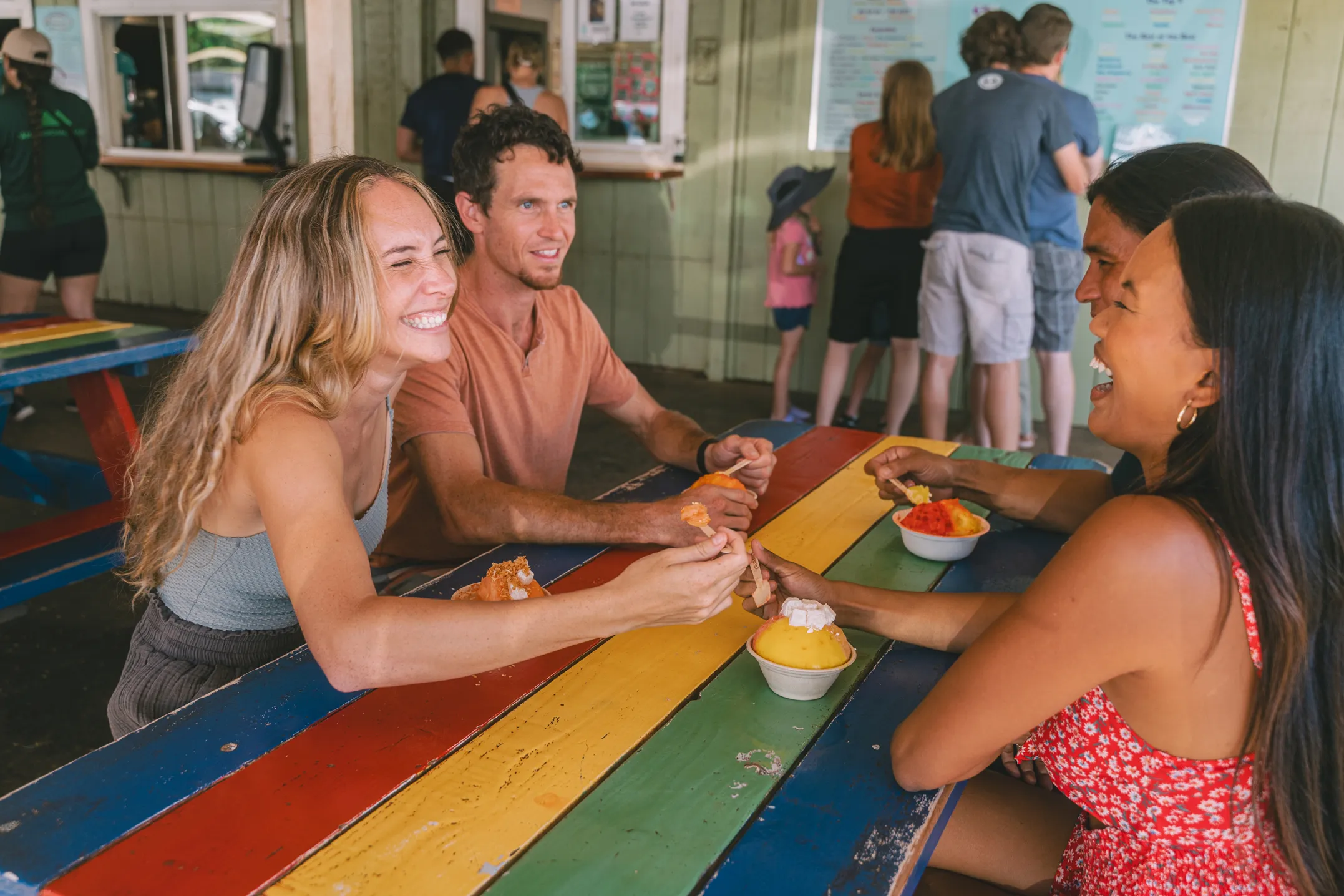 Three people eating shave ice together at a restaurant table with food and drinks.
