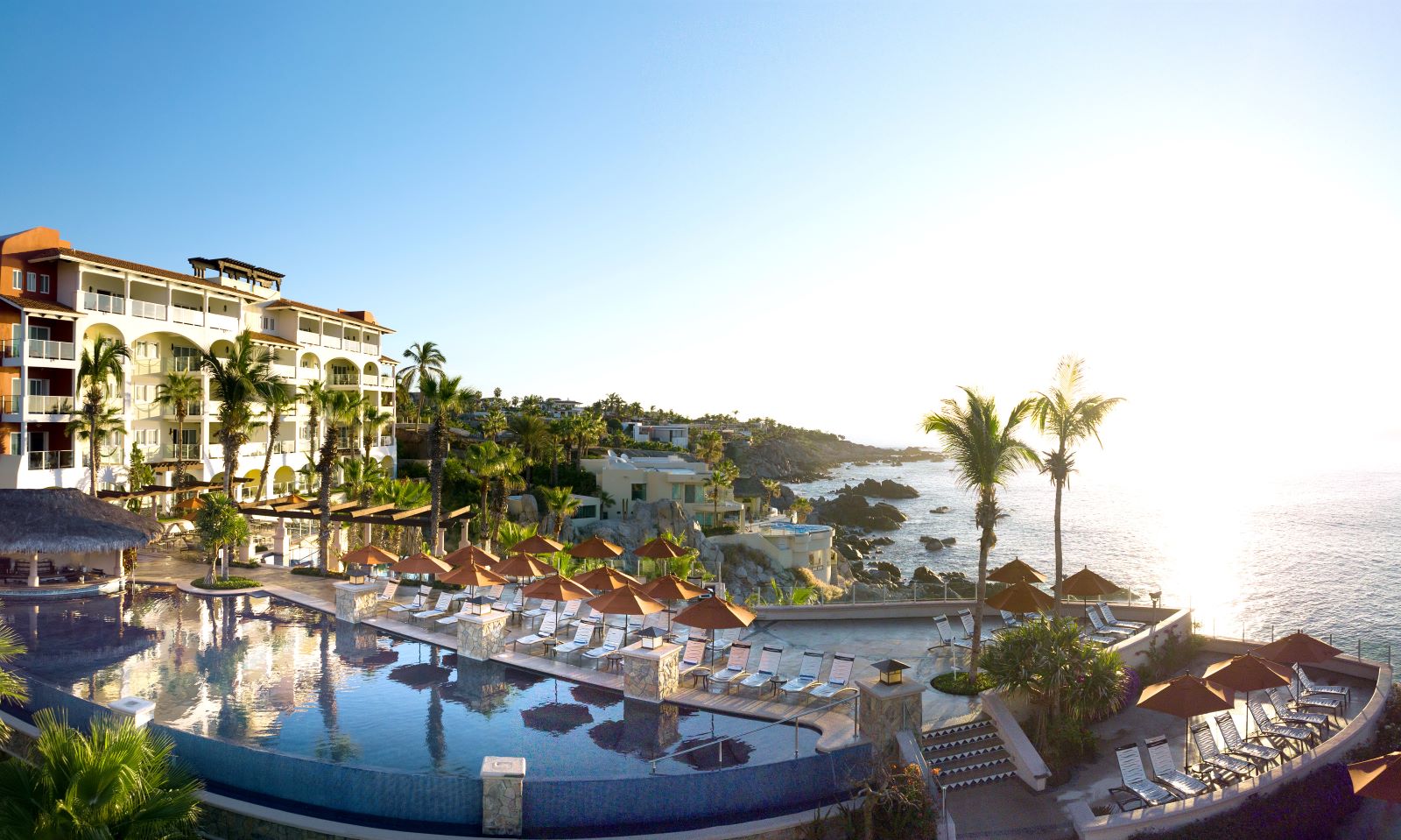 Cliffside view of a resort with palm trees, a pool, and the ocean