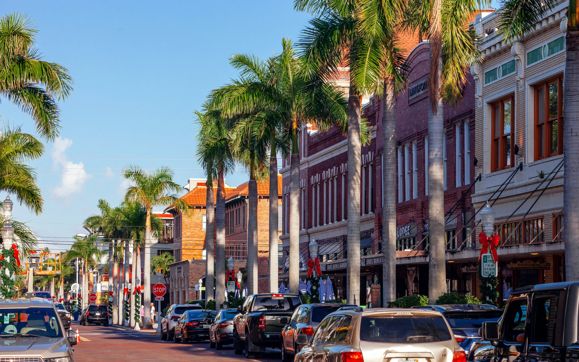 People walk along a colorful street lined with palm trees in the Fort Myers River District.