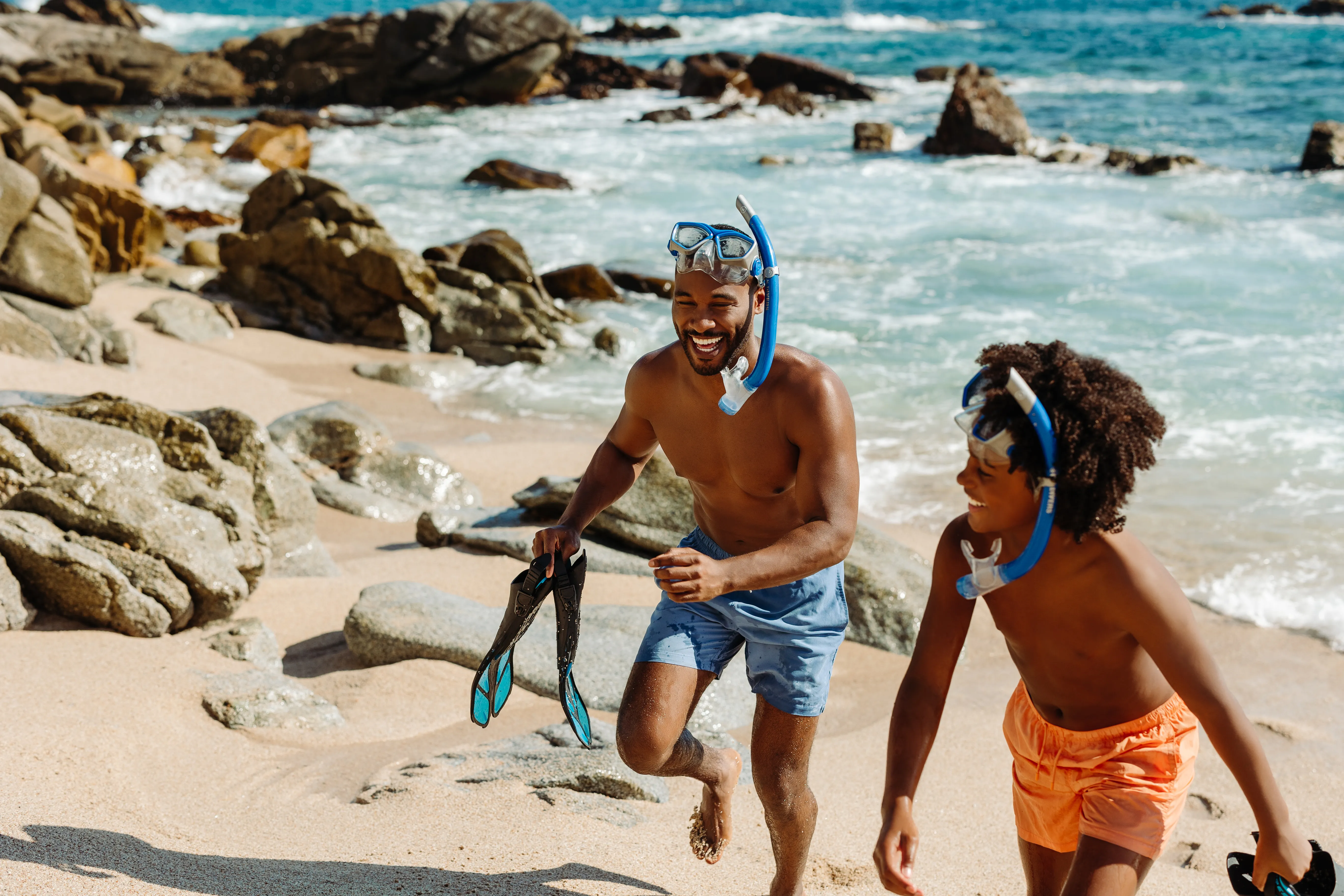 Father and son snorkeling near rocky shoreline.