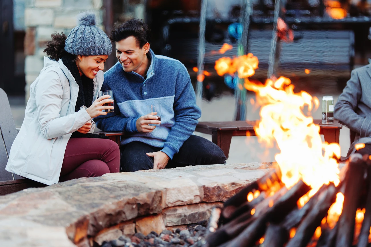 A couple gathered around a campfire at night, roasting marshmallows and socializing in a relaxed outdoor setting