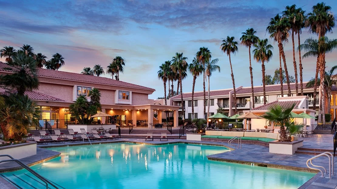 Poolside view with palm trees, chairs, and the resort at twilight