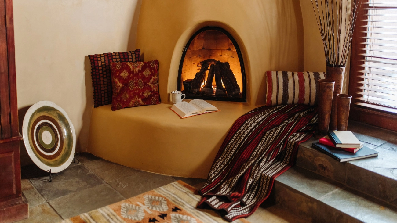 An open book and hot chocolate sit in front of a fireplace