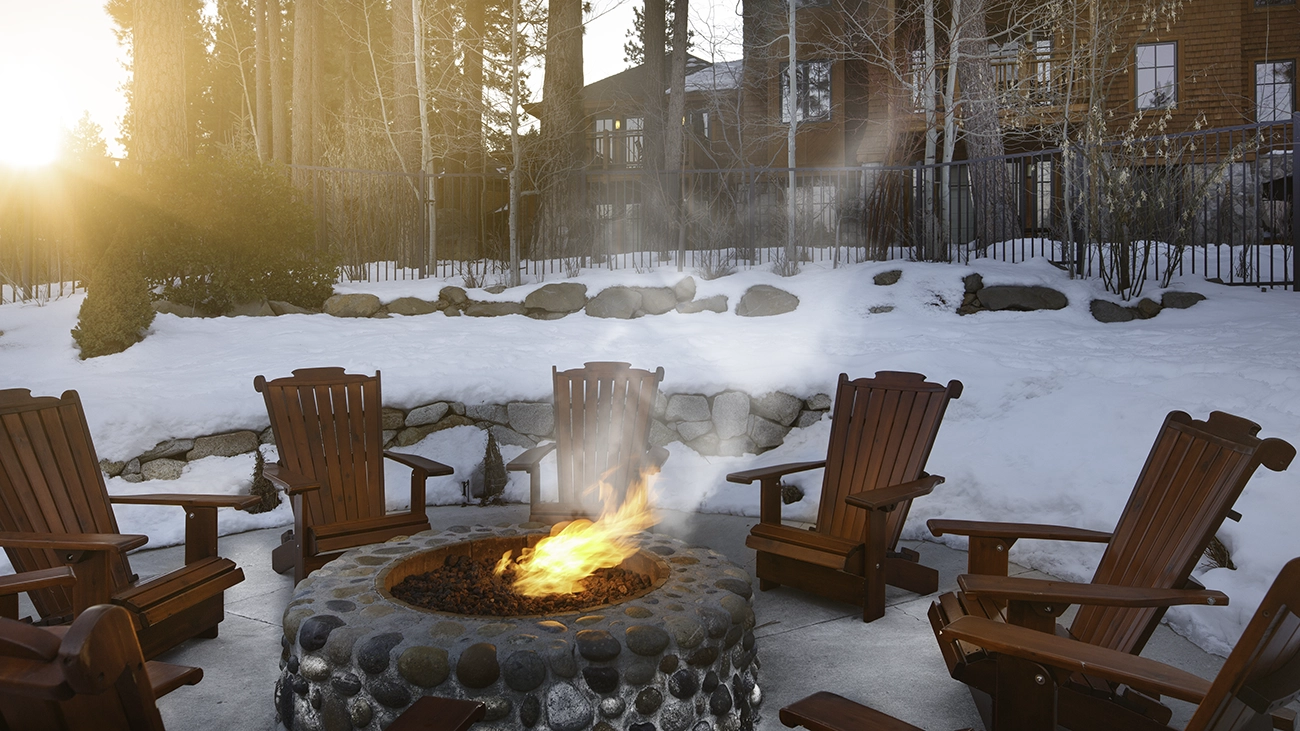 Smoke comes off a warm fire pit surrounded by chairs among the winter snow