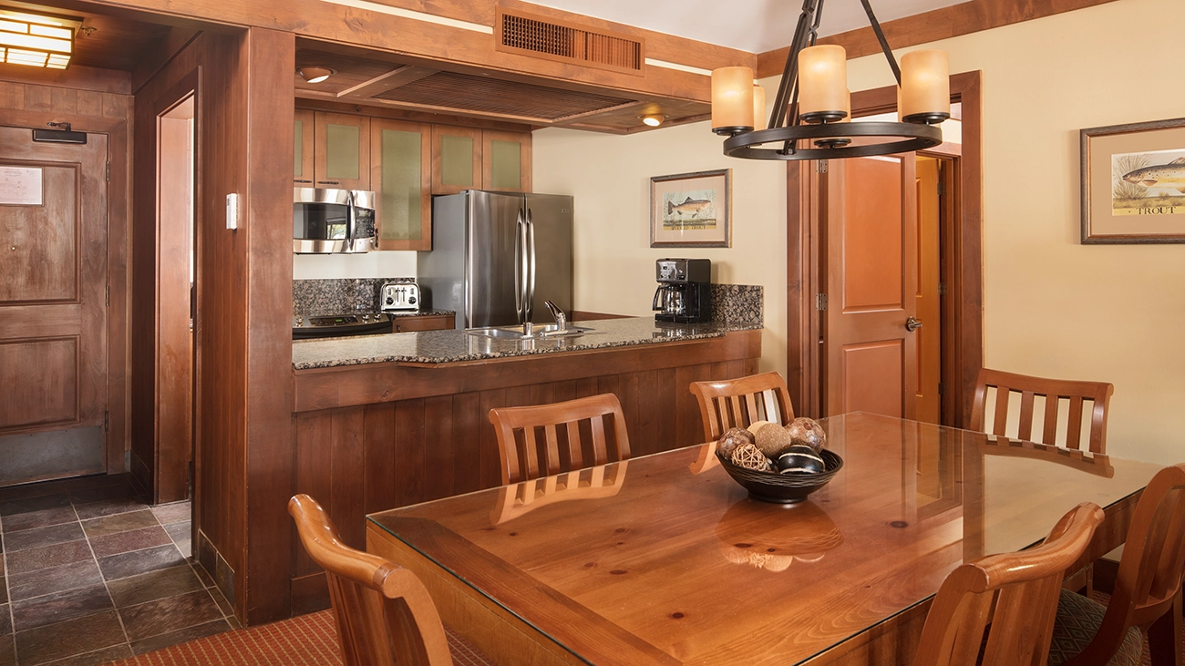 A dining table sits in front of a fully equipped kitchen