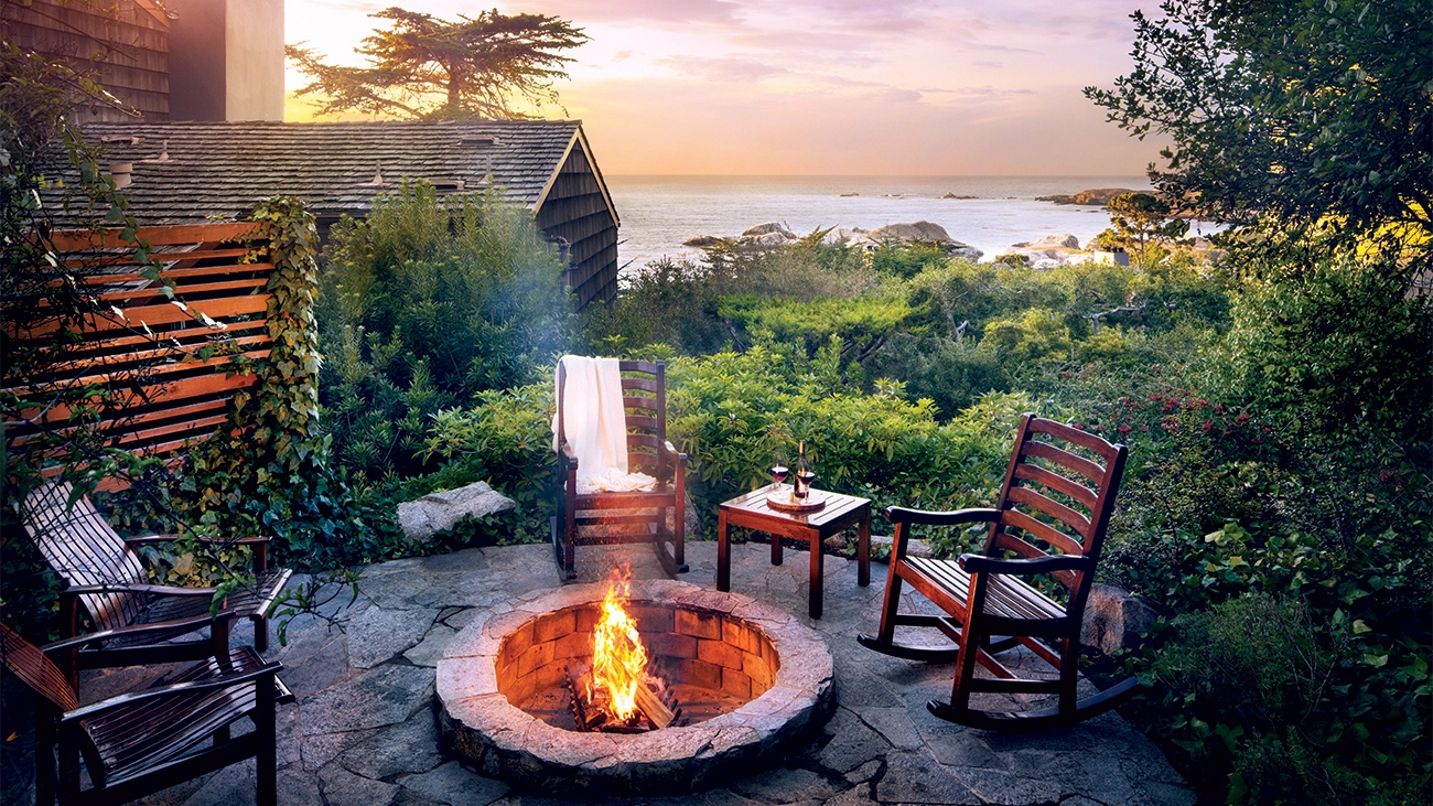 Rocking chairs surround a lit firepit in the middle of the trees at the Highlands Inn