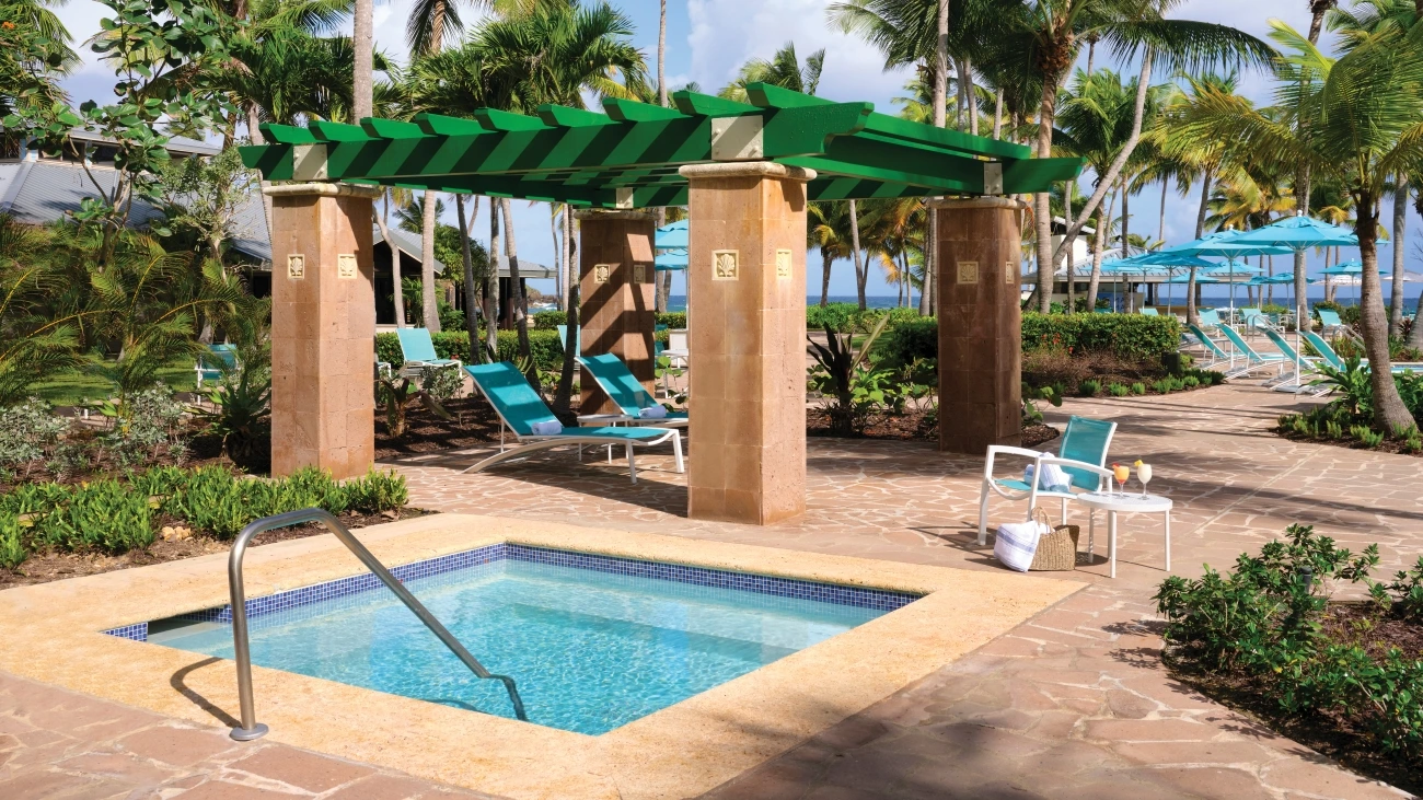 A whirlpool spa in the pool area with pergola, lounge chairs, and umbrellas