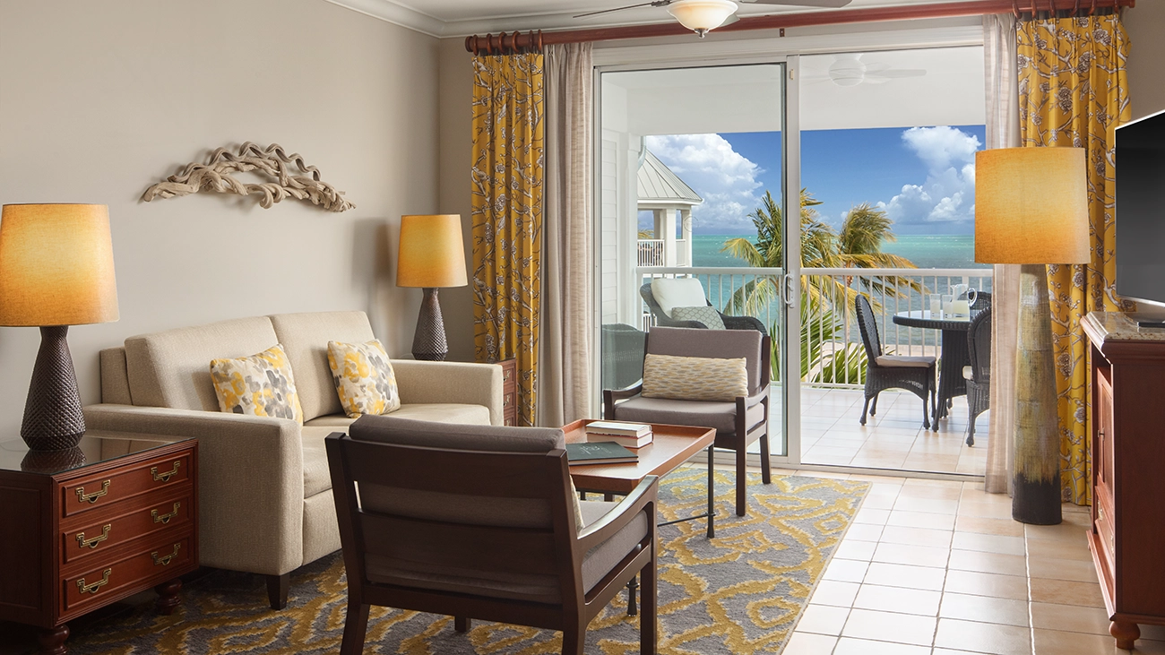 A couch and two chairs sit in a villa sitting area as the door of an attached outdoor patio is open