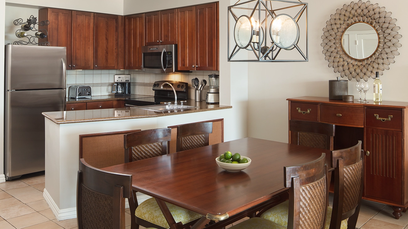 A dining table sits in front of a fully equipped kitchen