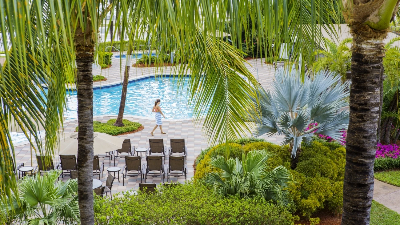 Woman in striped towel walks along a shimmering resort pool