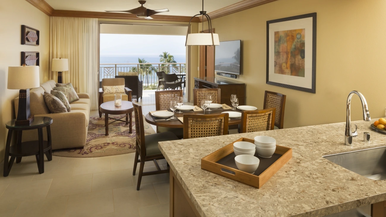 Couches, chairs, and a dining table are in the villas sitting area with the ocean outside