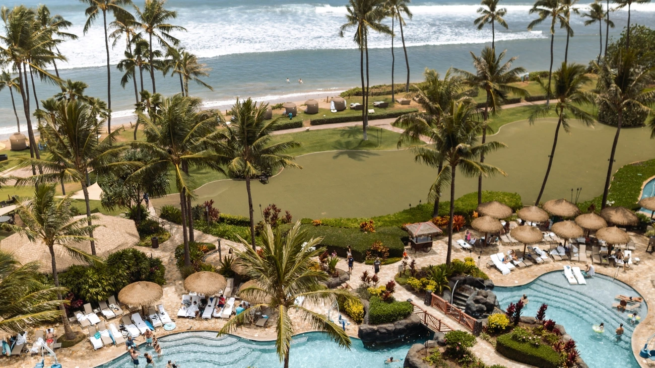 A green lawn sits in between a lively pool and an active ocean