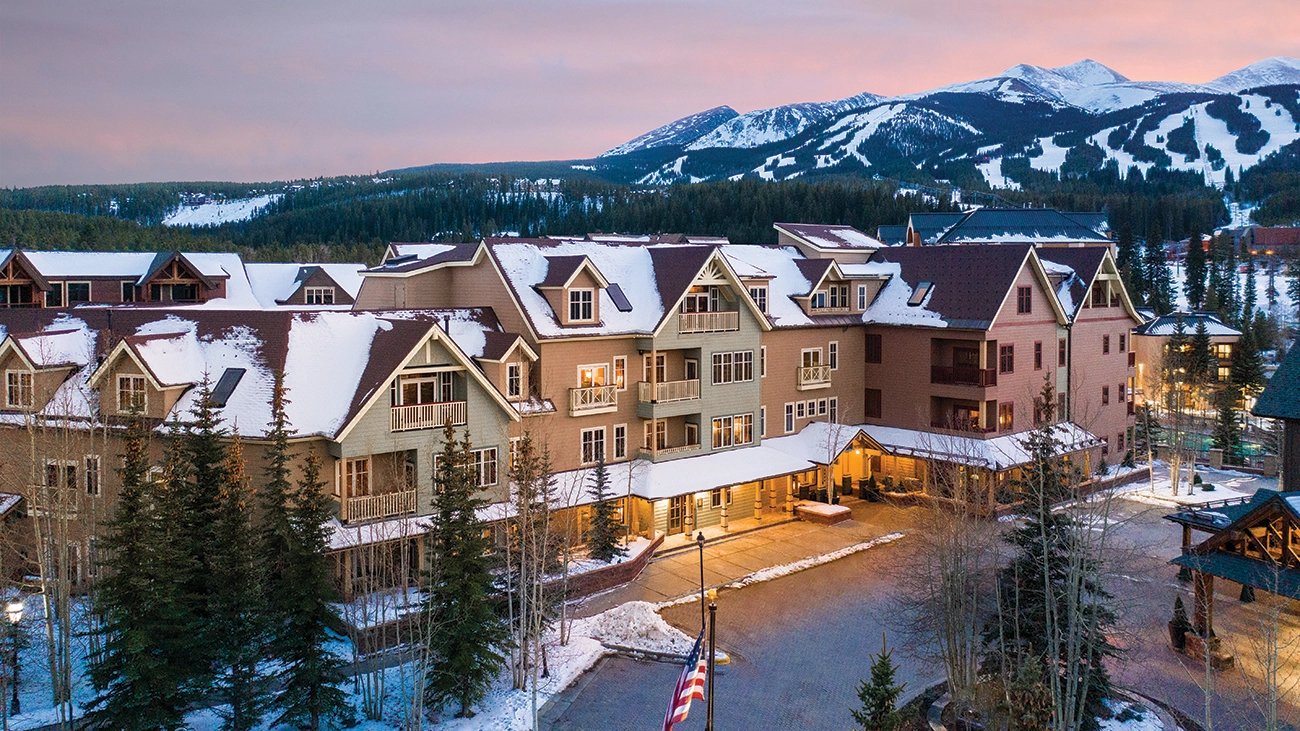 The resort's lights begin to shine as the sun dips below the snow-covered mountains