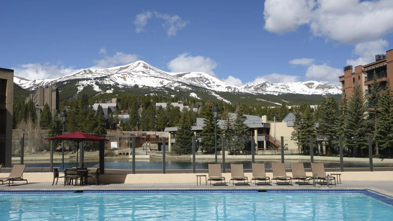 A large pool and a pair of hot tubs at Breckenridge Main Street Station sit under blue sky