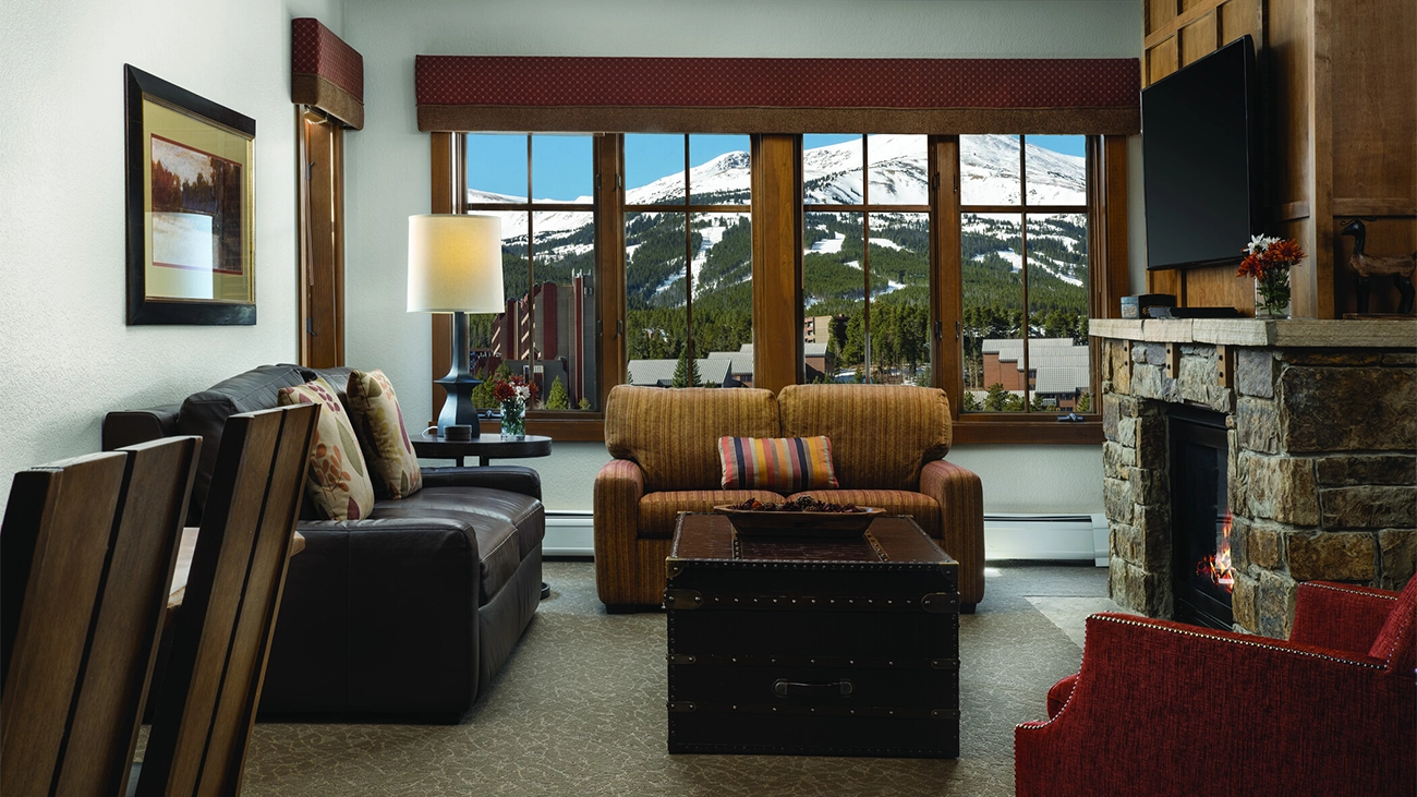A fire is burning in the resorts lobby under a stone hearth and next to wooden shelves