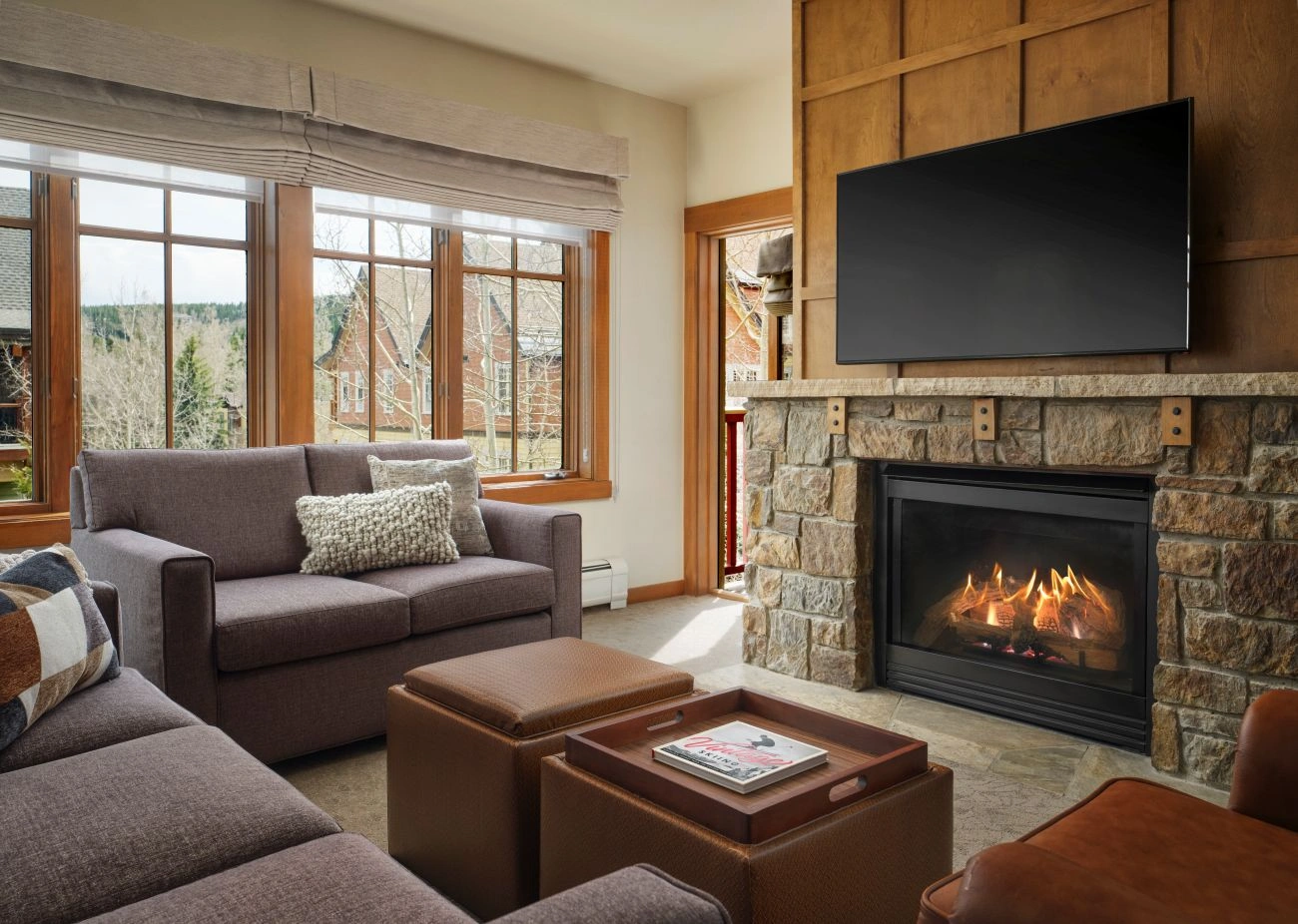 A fire is burning in the resorts lobby under a stone hearth and next to wooden shelves
