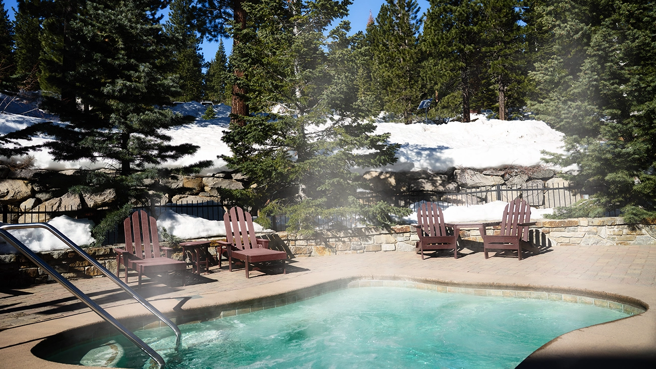 A steaming hot tub is surrounded by snow-covered rocks