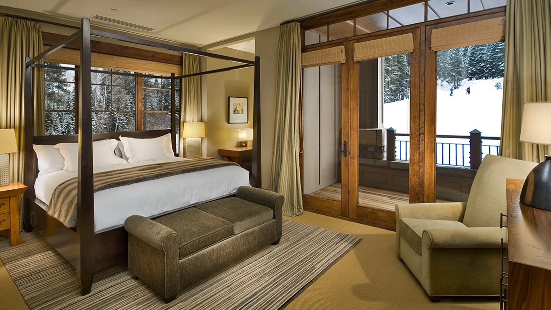 Interior of villa with four-poster bed, armchair and décor, with patio view of snowy slopes