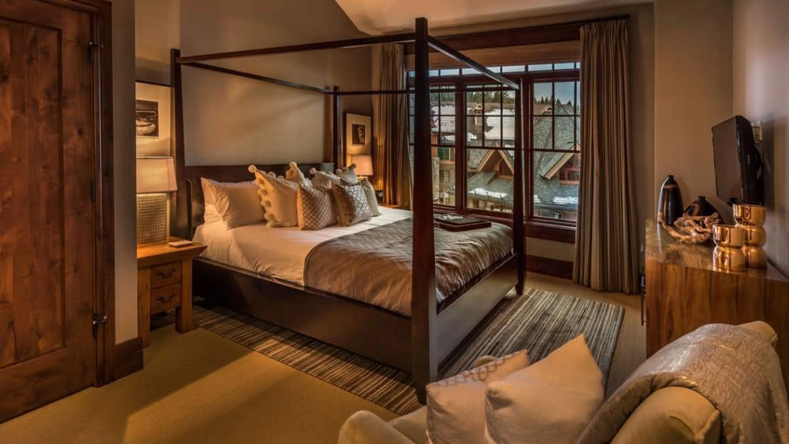 Interior of villa with four-poster bed, armchair and décor, with patio view of steepled roofs