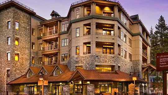 A resort with windows emitting golden light and evergreens in the background