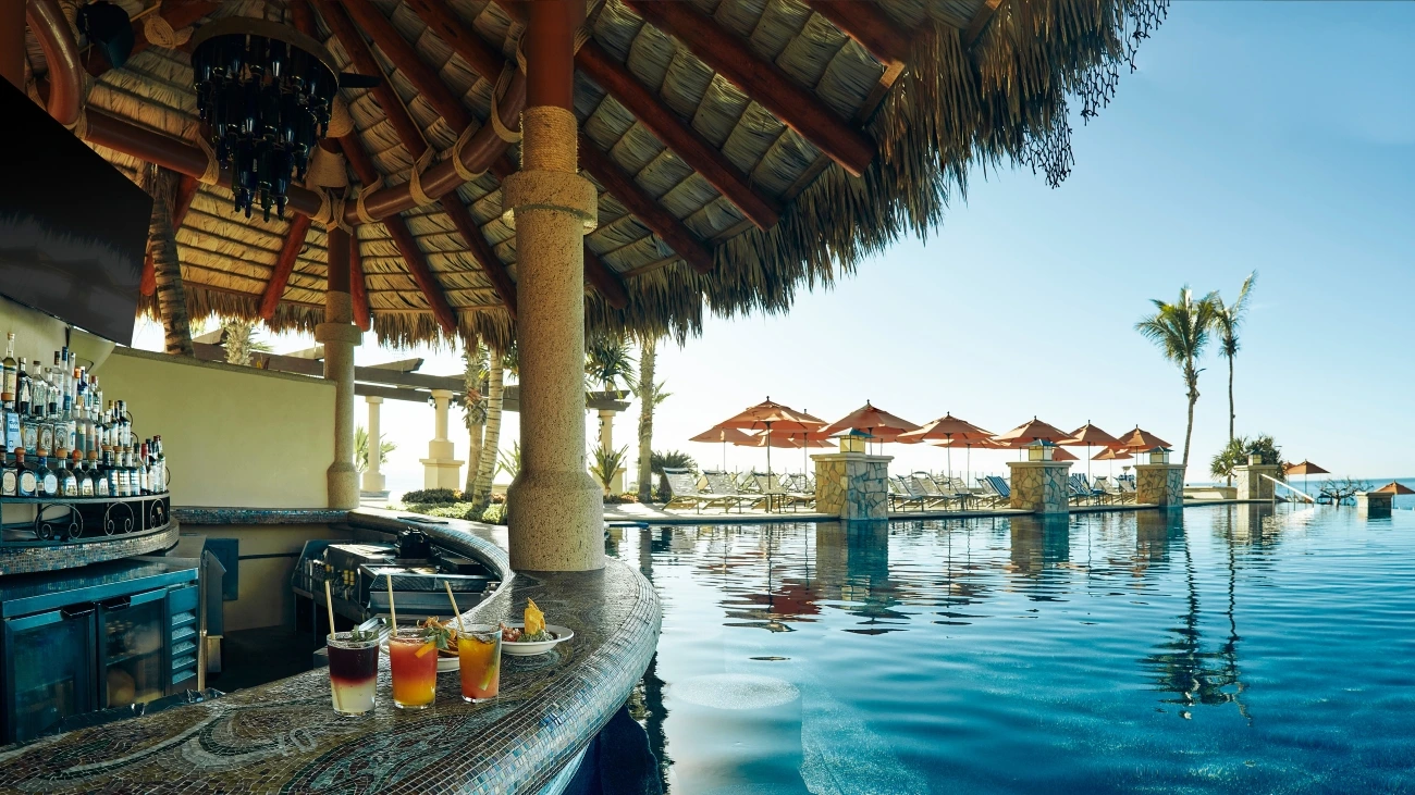 Drinks and food sit on the edge of a poolside, swim-up bar