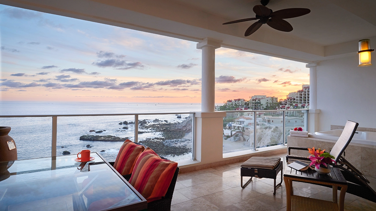 A villa balcony with a table and hot tub look out over the rocky coast