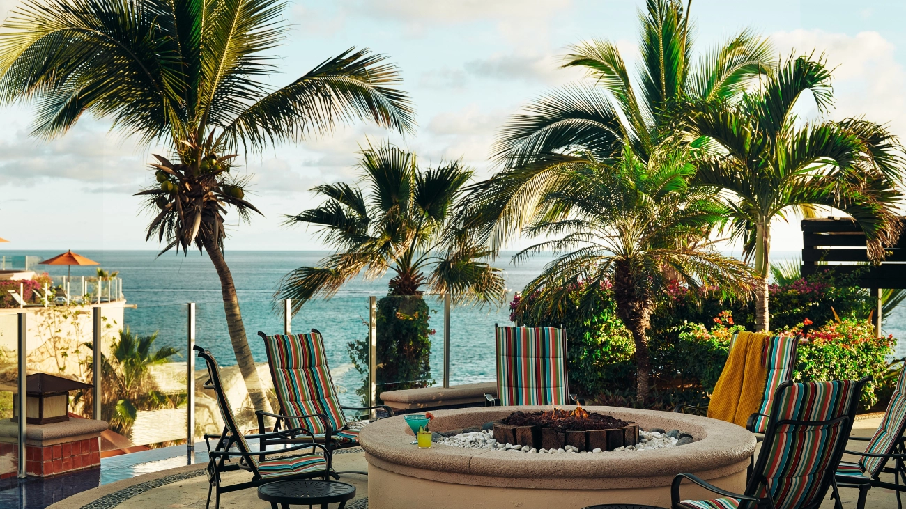 A lit firepit with drinks around it overlook the ocean