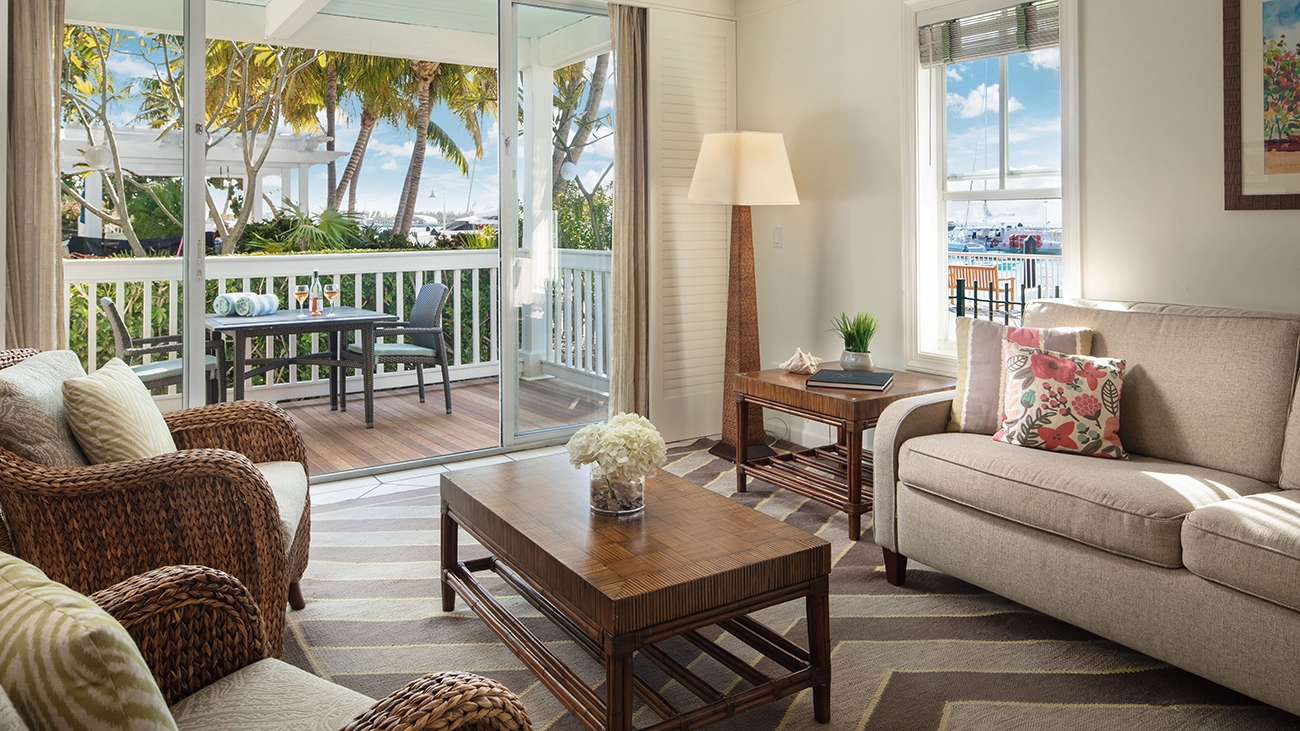 A couch and two chairs sit in a villa sitting area as the door of an attached outdoor patio is open