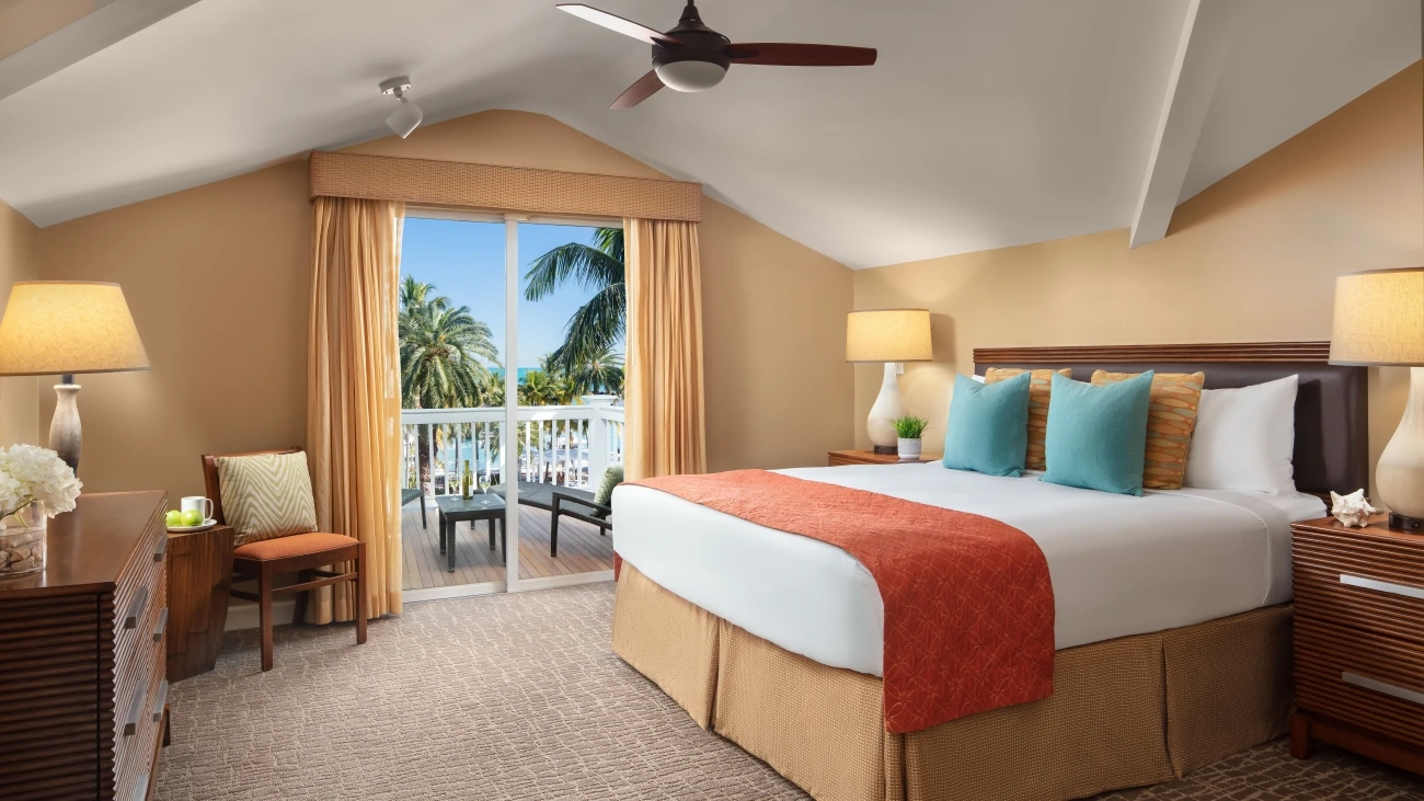 Colorful decorations and linens line the king size bed as an outdoor patio door is open