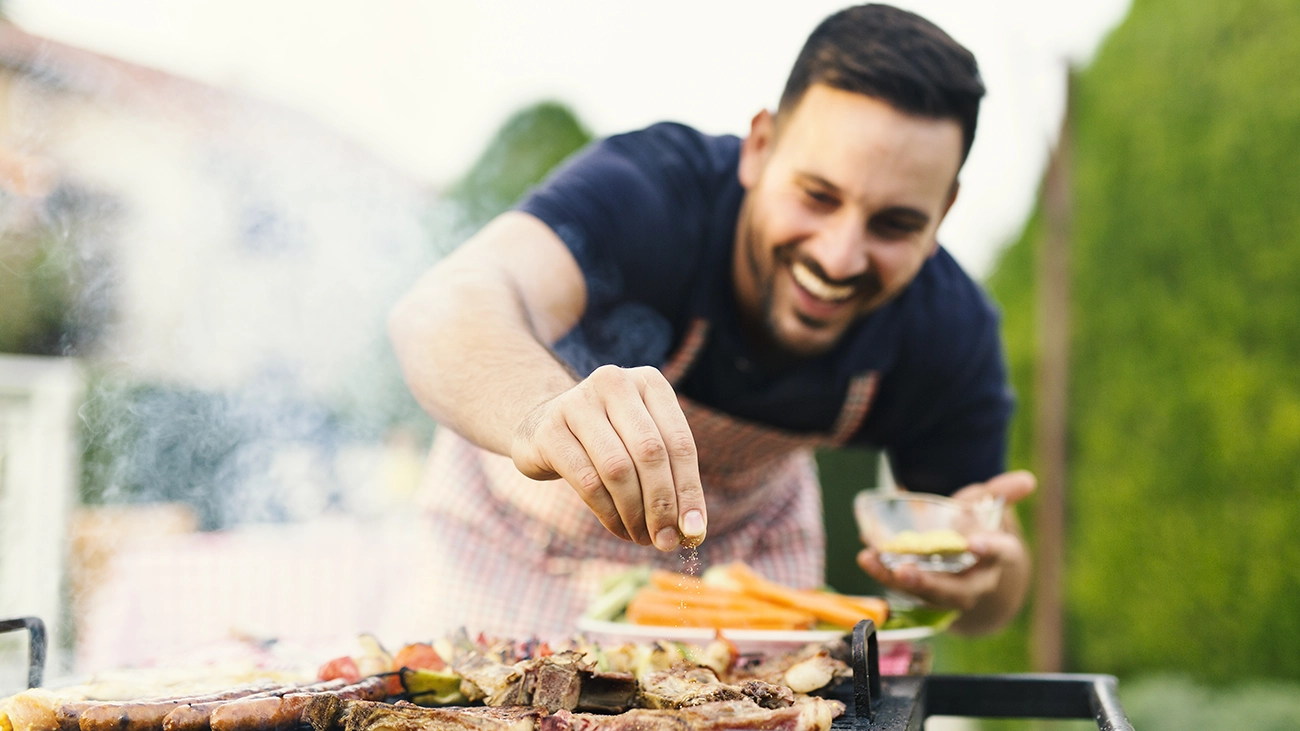 A smiling man seasoning steaks on a grill