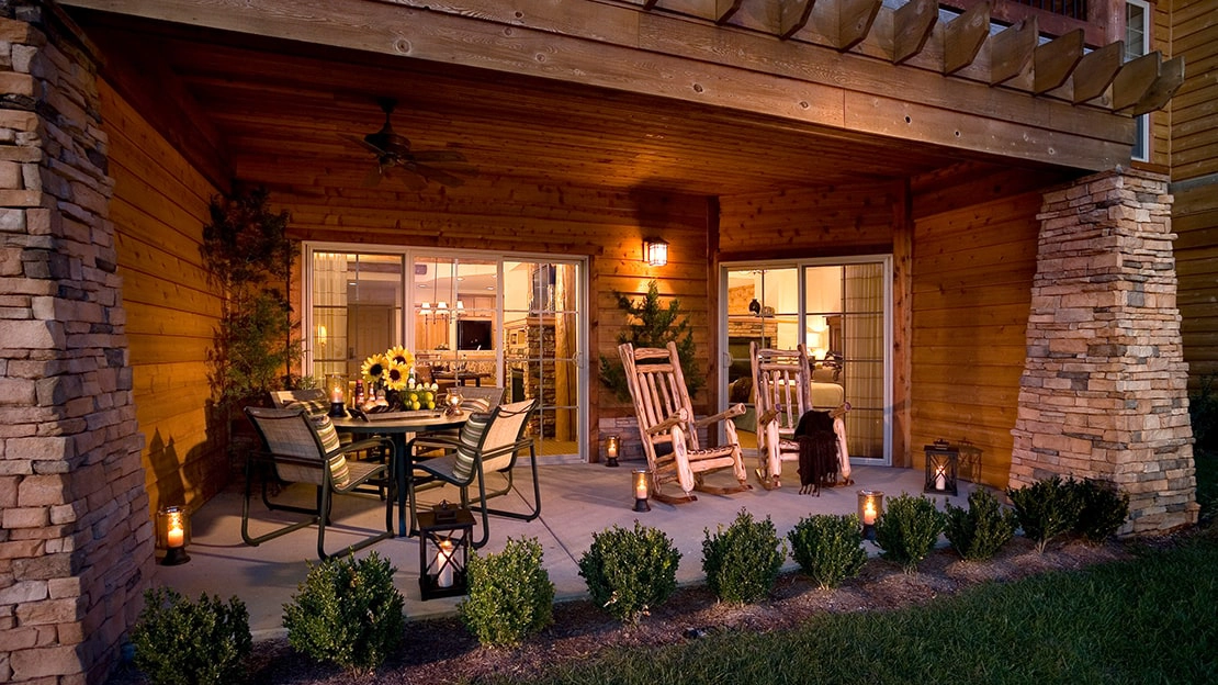 Wood-carved rocking chairs and a dining area sit under the lights of an outdoor porch at night