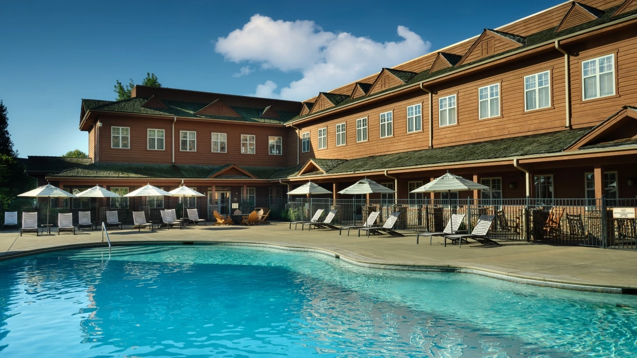 Poolside view at a resort with lounge chairs, tables, and umbrellas