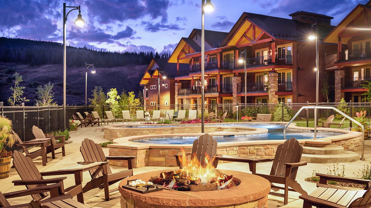 A firepit is lit in front of a pool and resort