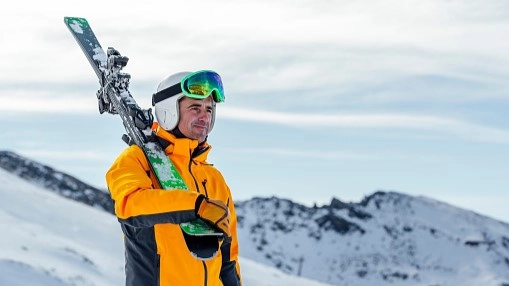 Man in yellow ski jacket holds his skis over his shoulder, eyeing the next mountain pass