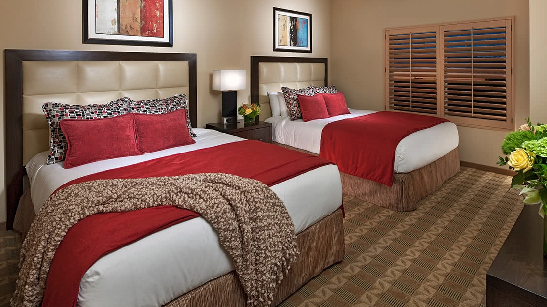 View of a villa bedroom with two beds with red and tan accents